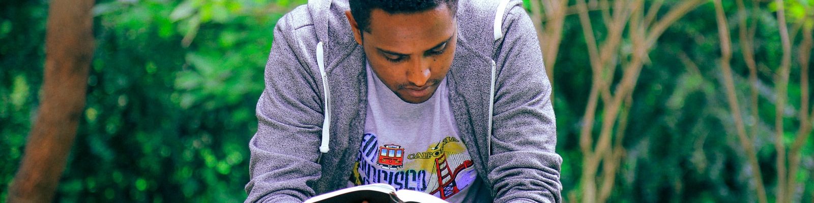 man sitting on concrete bench reading book
